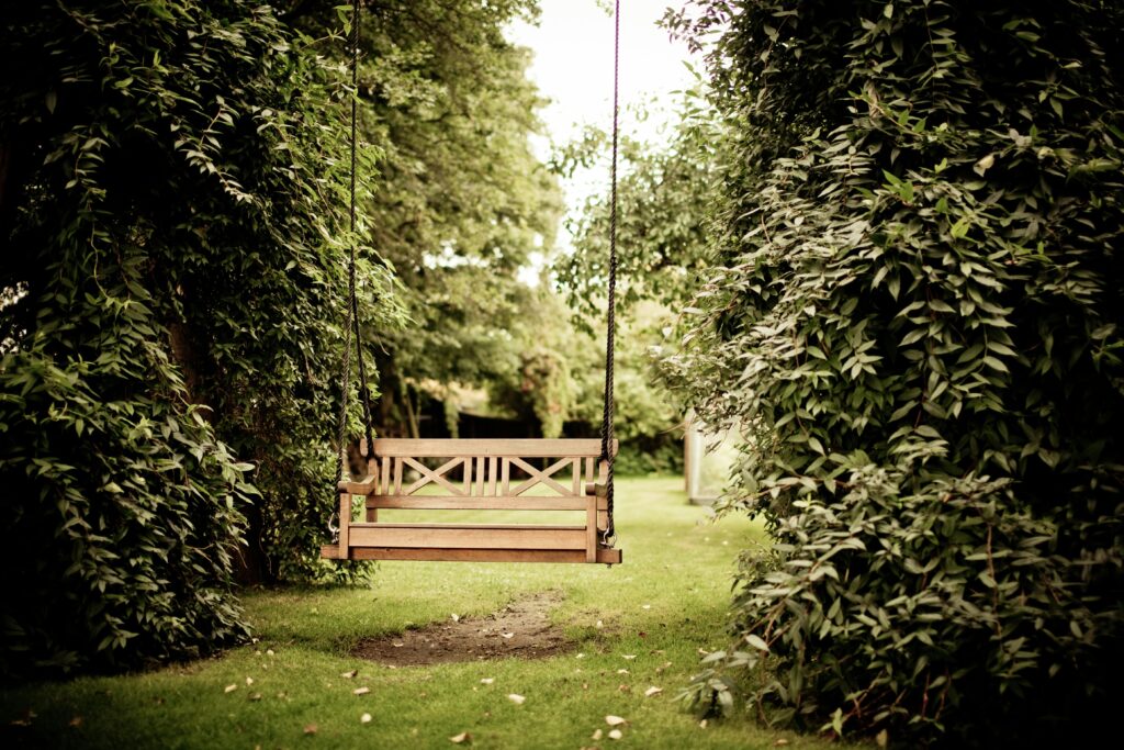 A tranquil wooden swing hanging in a verdant garden setting, ideal for relaxation.